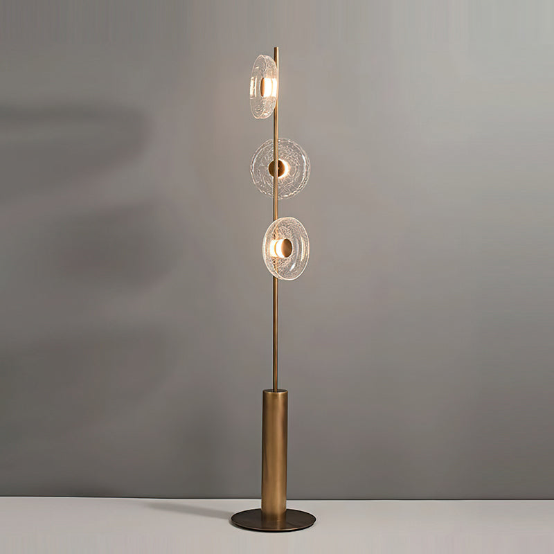 Clérachic floor lamp with three clear crackle glass discs lit, standing on a pale surface in front of a soft grey wall.