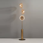 This Clérachic floor lamp lit against a grey wall, with the lowest disc glowing as a ring and two amber discs above.
