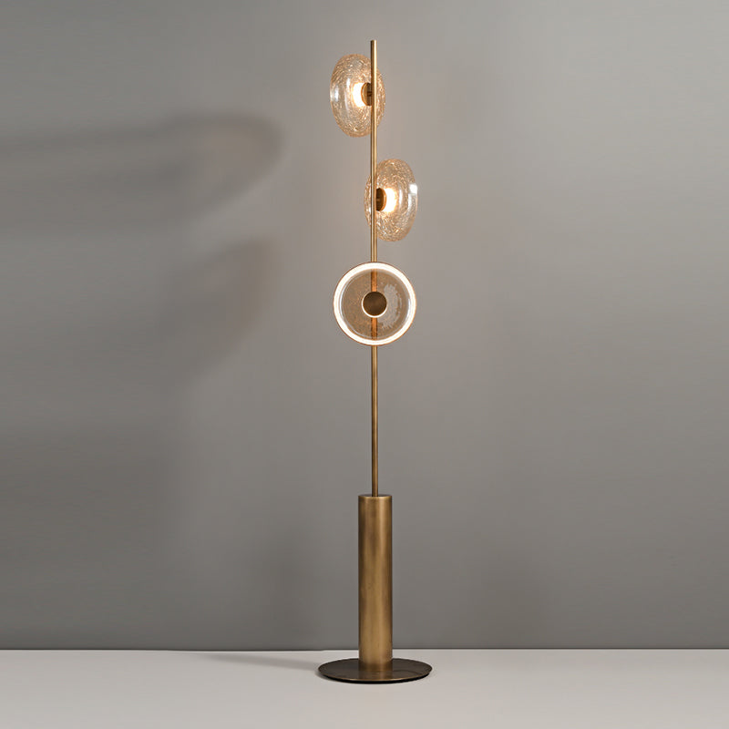 This Clérachic floor lamp lit against a grey wall, with the lowest disc glowing as a ring and two amber discs above.