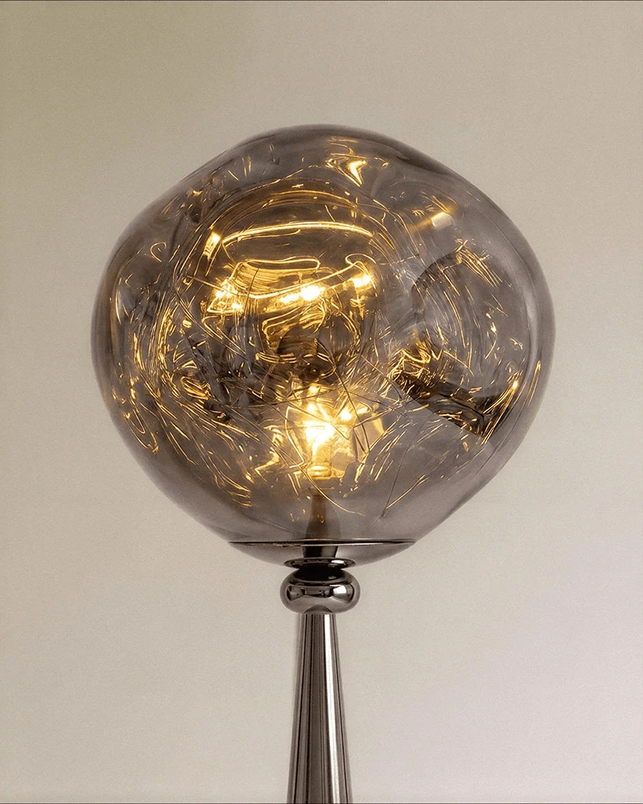 Clérachic close-up of the rippled grey shade glowing warm around the bulb, above a polished gunmetal neck.