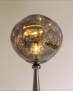 Clérachic close-up of the rippled grey shade glowing warm around the bulb, above a polished gunmetal neck.
