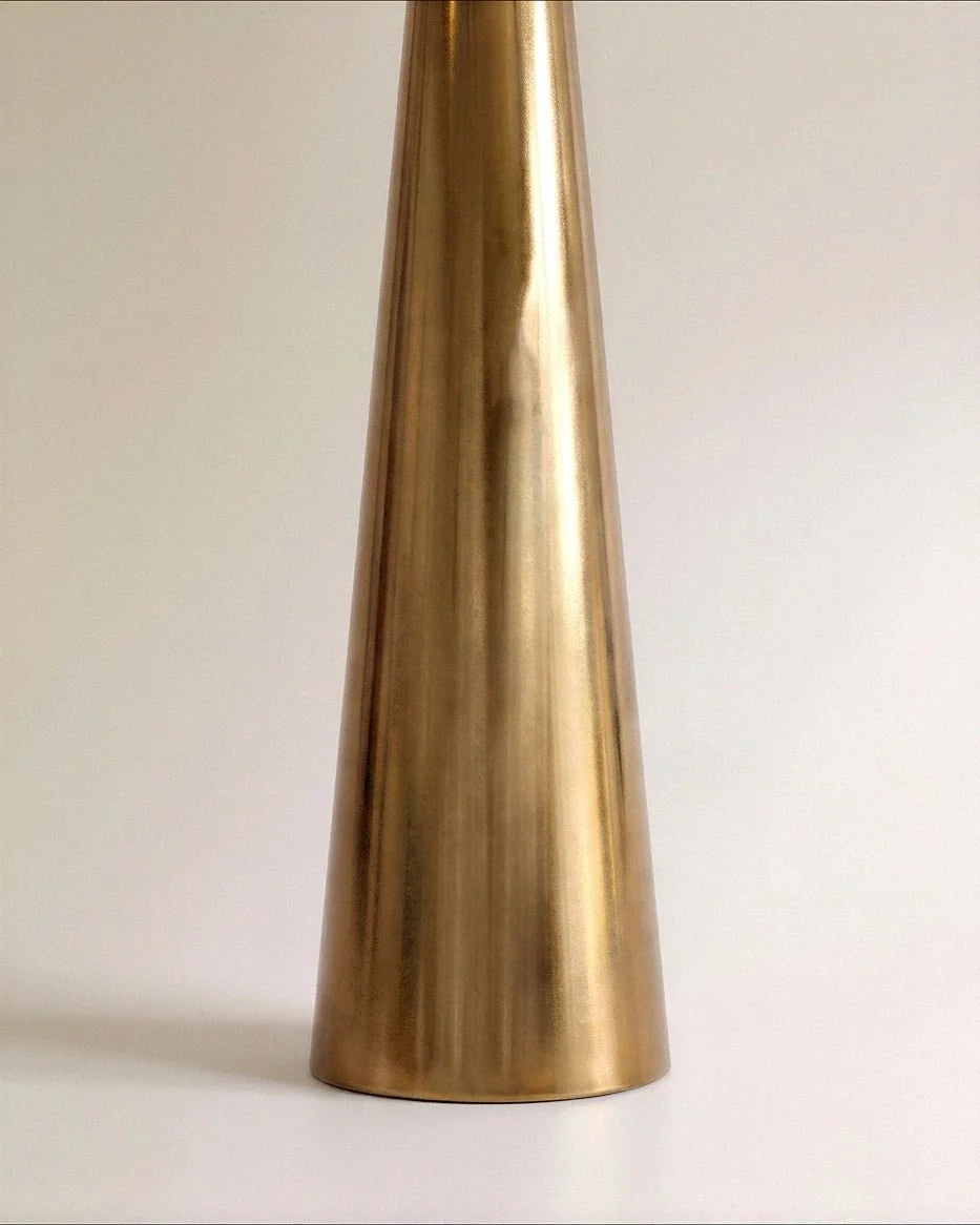 Clérachic base of the cone stem in polished gold with a soft brushed sheen, standing on a pale studio floor.