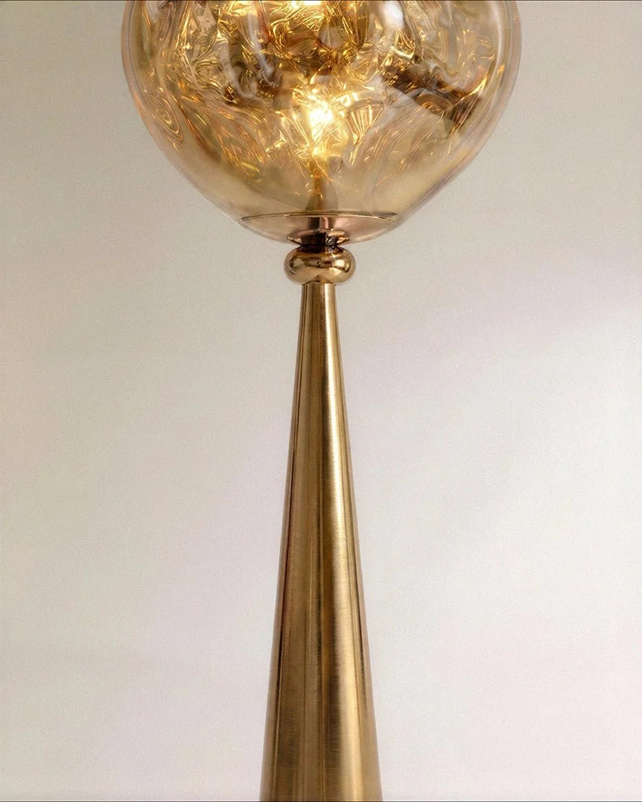 Clérachic brushed gold cone stem with a ball joint, topped by the glowing rippled amber shade, close view.