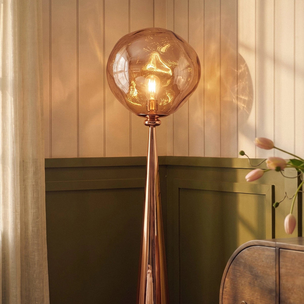 Clérachic rose gold floor lamp with a rippled amber shade lit warm against panelled walls beside an olive green cabinet.