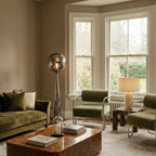 Clérachic chrome floor lamp with a rippled grey shade in a living room with olive velvet seating and a burr wood table.