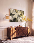 Clérachic floor lamp in matt white with a brass arm and linen drum shade, standing beside a burr-wood sideboard under a framed painting.