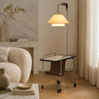 Nickel-framed Clérachic floor lamp with a black glass tabletop beside a marble fireplace, a bouclé armchair and a sunlit curtain.