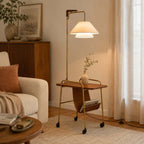 Brass-framed Clérachic floor lamp with a leather sling and a small vase on its table, beside a rust cushion on a cream sofa.