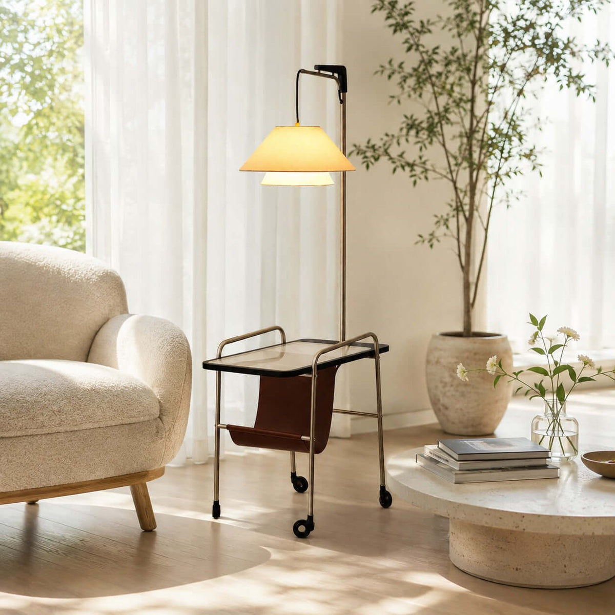Clérachic floor lamp with a nickel frame in front of sheer curtains, beside a bouclé armchair, a tall plant and a low stone coffee table.