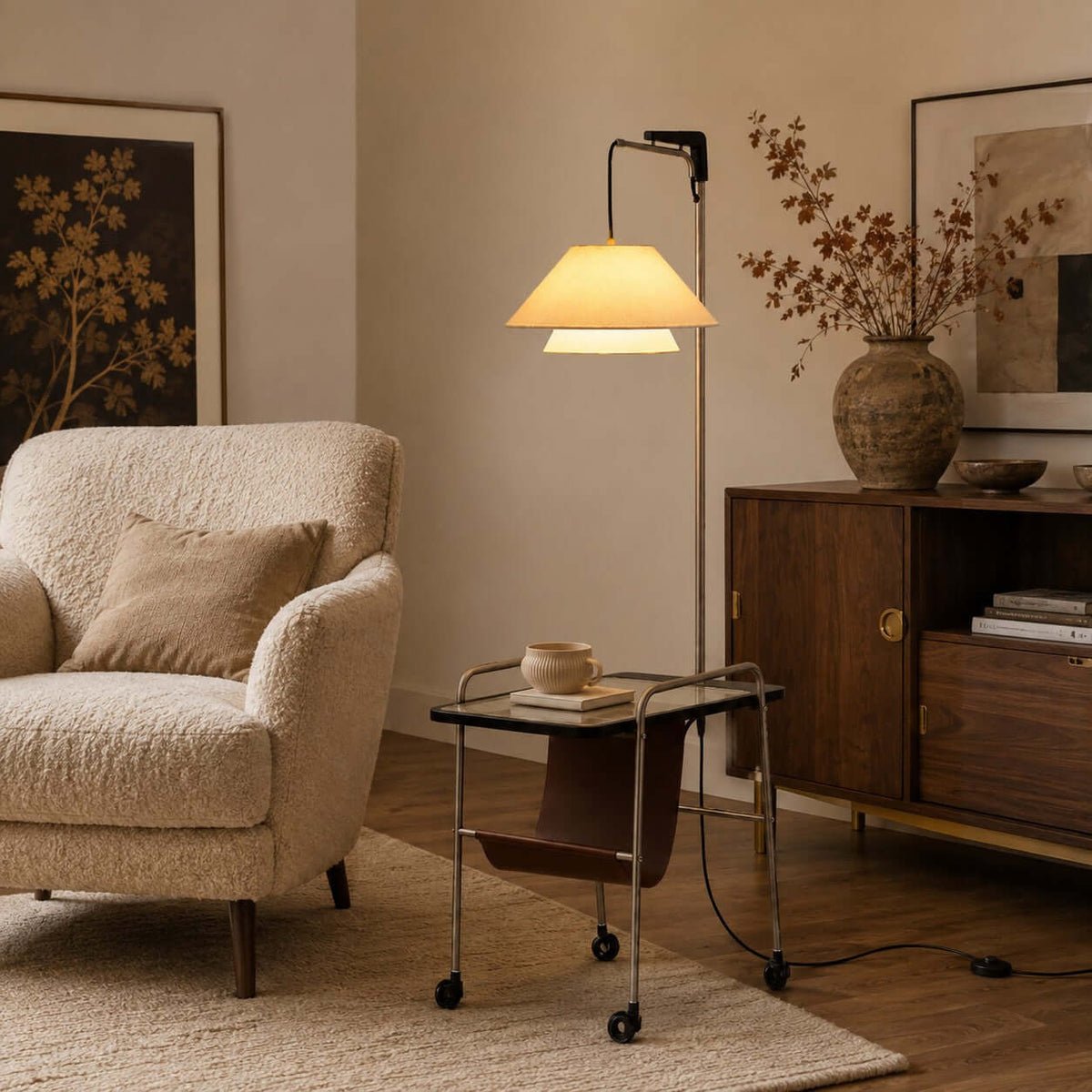 Lit nickel and black Clérachic floor lamp holding a cup and books on its tabletop, beside a bouclé armchair and a walnut cabinet.