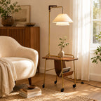 Brass and brown Clérachic floor lamp holding a small vase on its tabletop, beside a cream armchair, a fluted cabinet and a bright window.