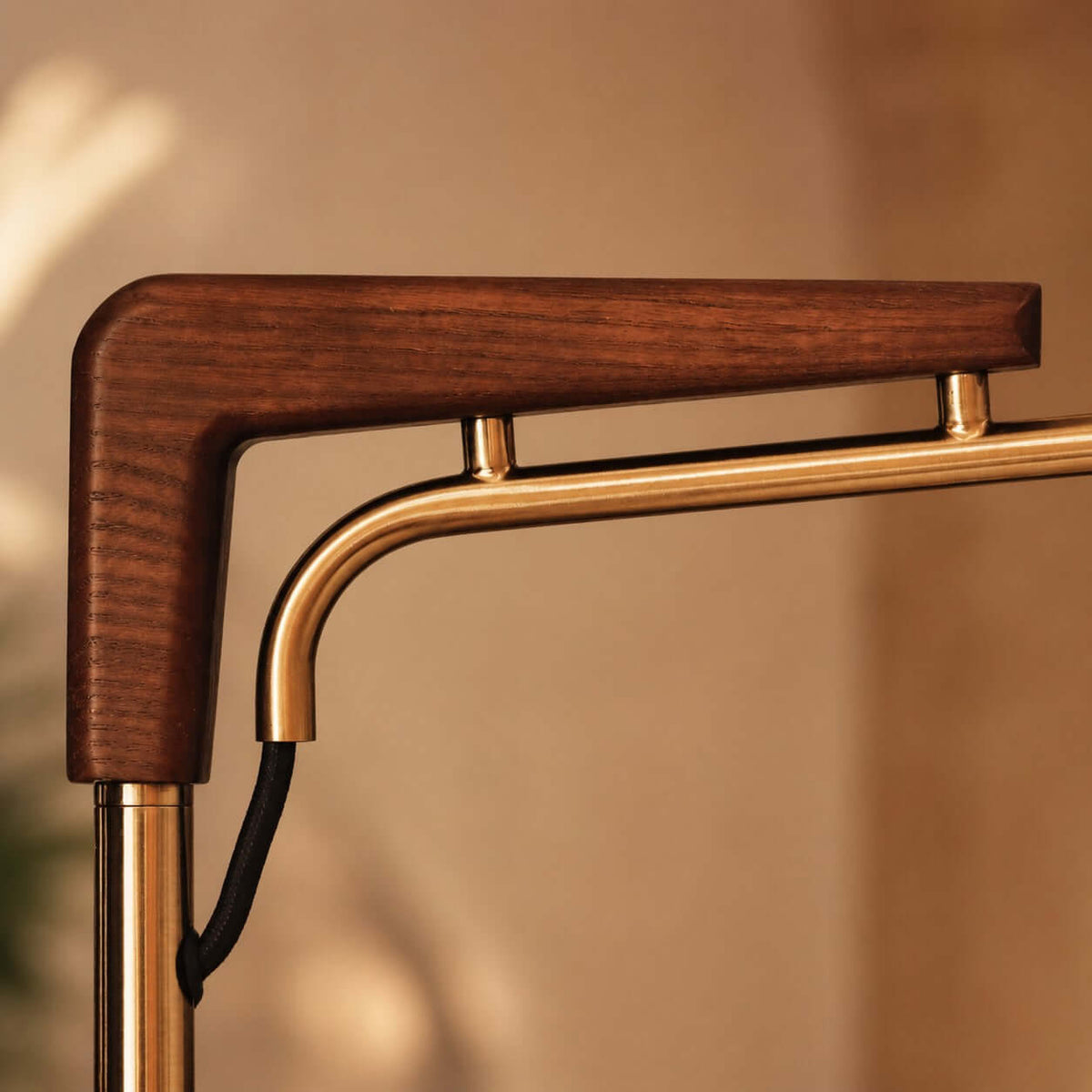 Close view of the walnut-toned wooden bracket and the brass tube it joins at the top of the stem, on this Clérachic floor lamp.