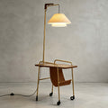 Clérachic floor lamp with a brass stem, a brown tabletop and a tan leather sling, with its cord trailing on the floor beside it.