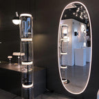 Clérachic glass floor lamp lit in a showroom beside a tall oval mirror, with a ring of light at each joint of the glass.