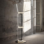 A Clérachic glass floor lamp with a cone shade and two cylinders in a room with weathered walls and a shaft of sunlight.