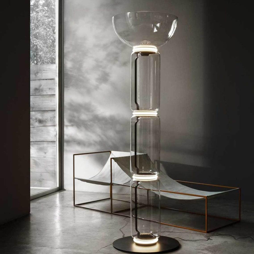 Clérachic glass floor lamp with a bowl shade in a concrete room, beside a low metal-framed lounger and a tall window.