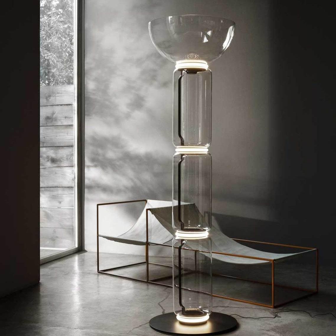 Clérachic glass floor lamp with a bowl shade in a concrete room, beside a low metal-framed lounger and a tall window.