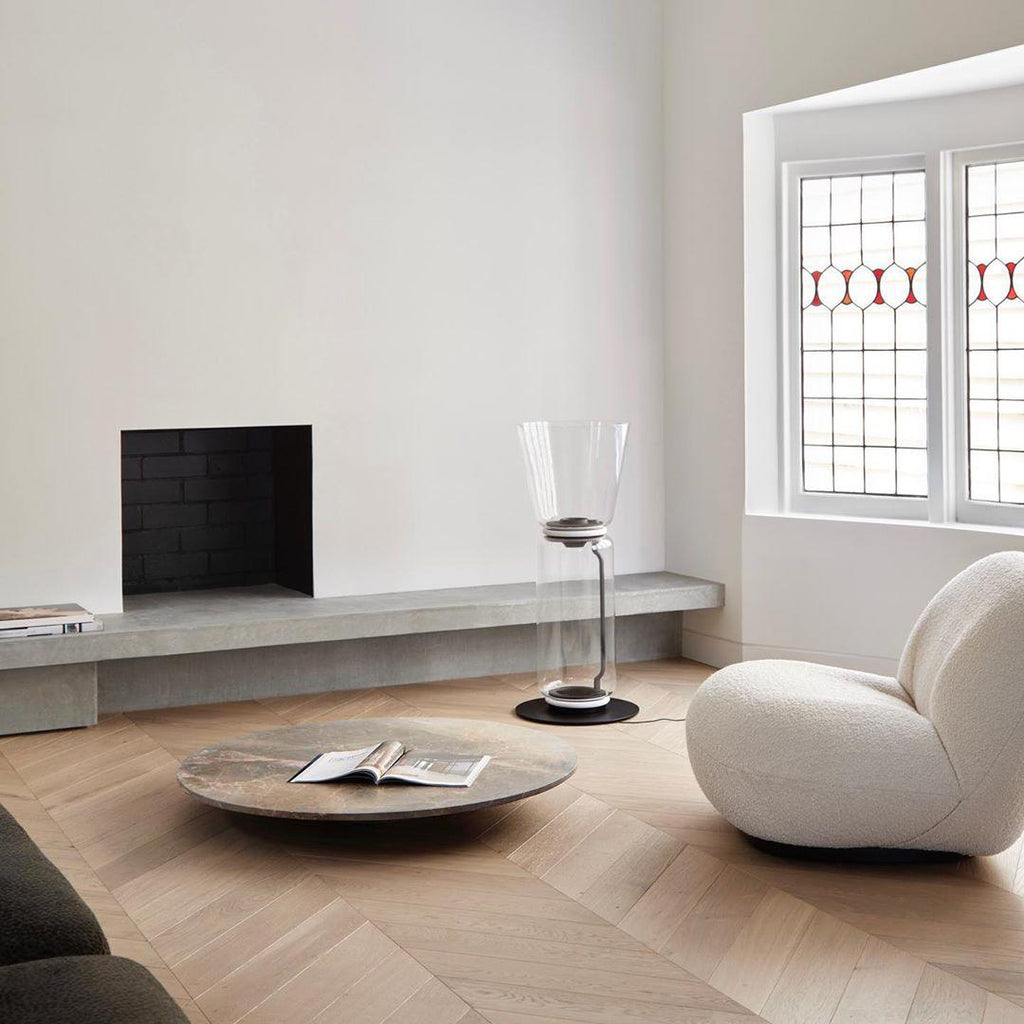 Small Clérachic cone-shade glass floor lamp near a fireplace, a stone slab seat and a low round table, with a cream armchair at right.