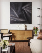 Clérachic glass floor lamp at the edge of a sitting room, beside a large dark artwork, a wooden sideboard and a bunch of tulips.