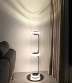 Clérachic glass floor lamp with a cone shade lit in a corner beside a grey armchair and a long taupe curtain.
