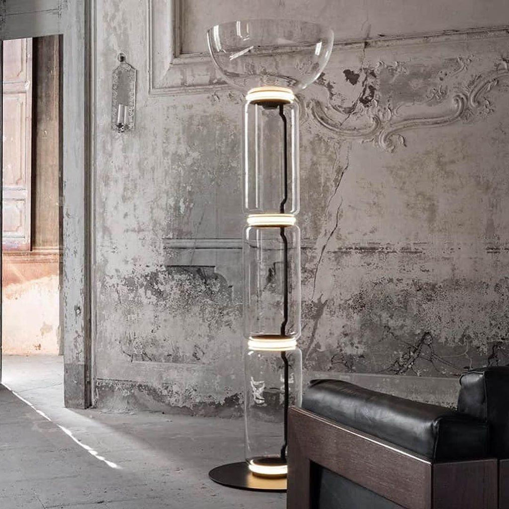 A Clérachic glass floor lamp with a bowl shade against a crumbling plaster wall, with a dark leather armchair at the right.