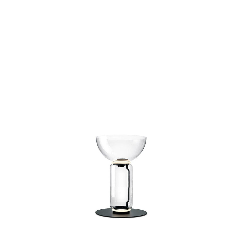 Short Clérachic glass floor lamp with a bowl shade over one clear cylinder, on a round black base against white.