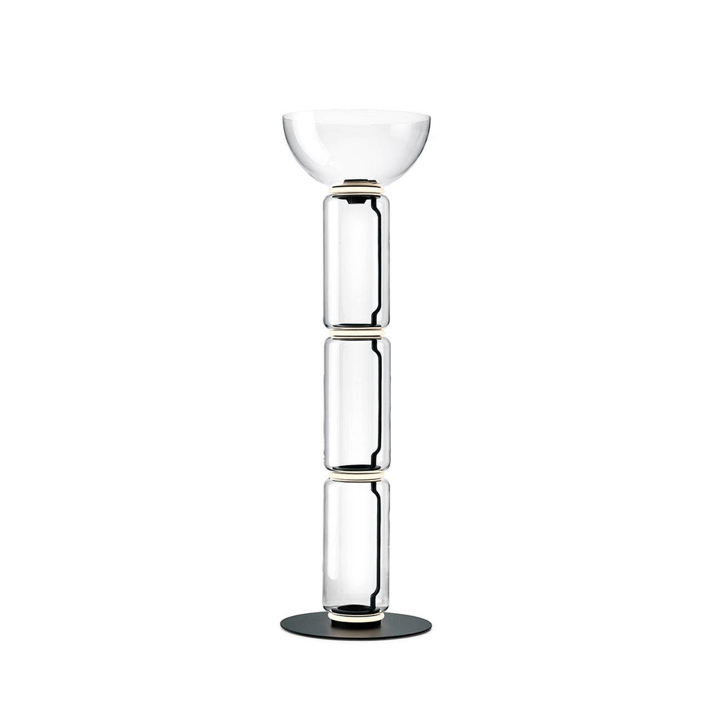 A Clérachic glass floor lamp with a bowl shade over three clear cylinders and a thin glowing ring at each joint, on white.