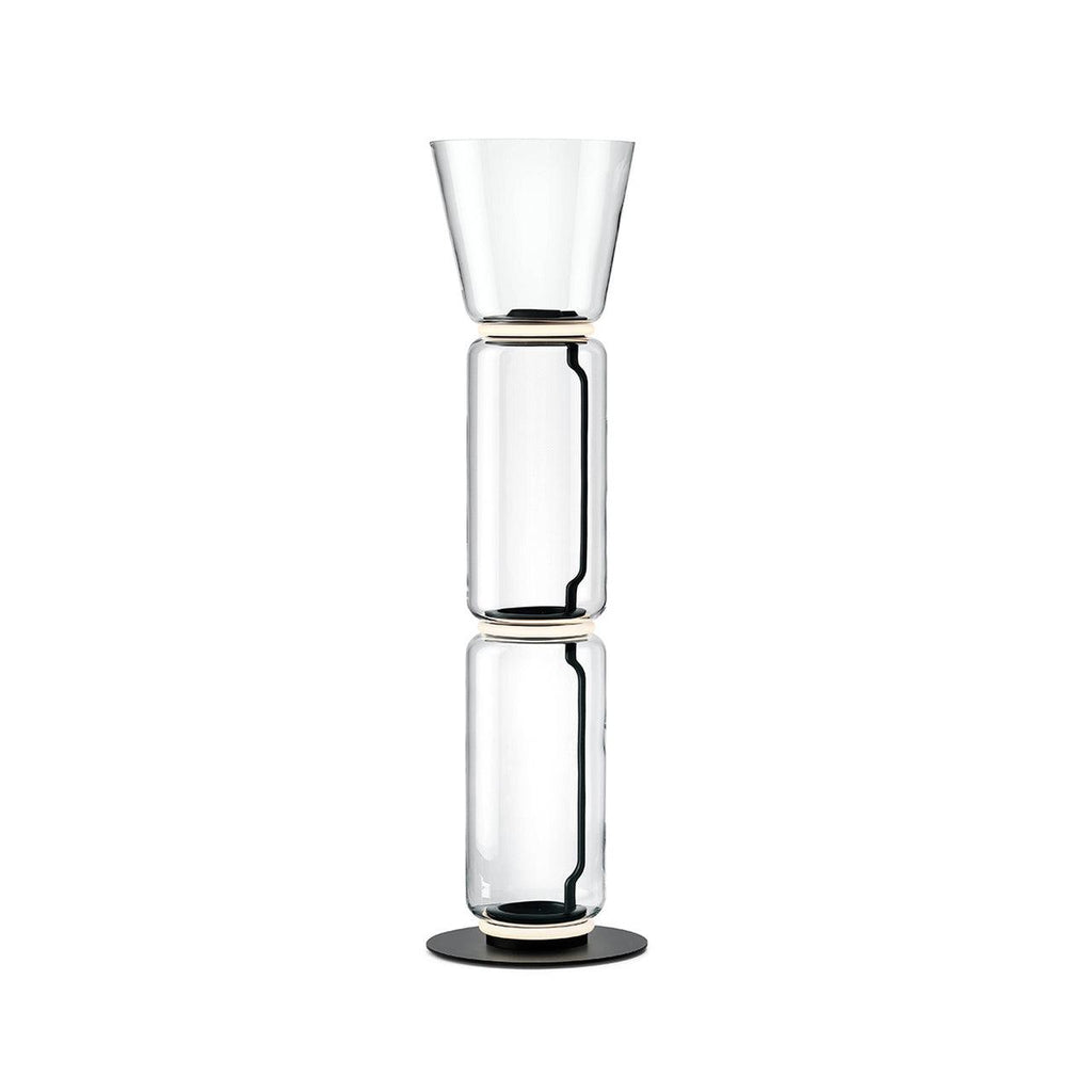 A Clérachic glass floor lamp with a cone shade over two clear cylinders and a black base, on a plain white backdrop.