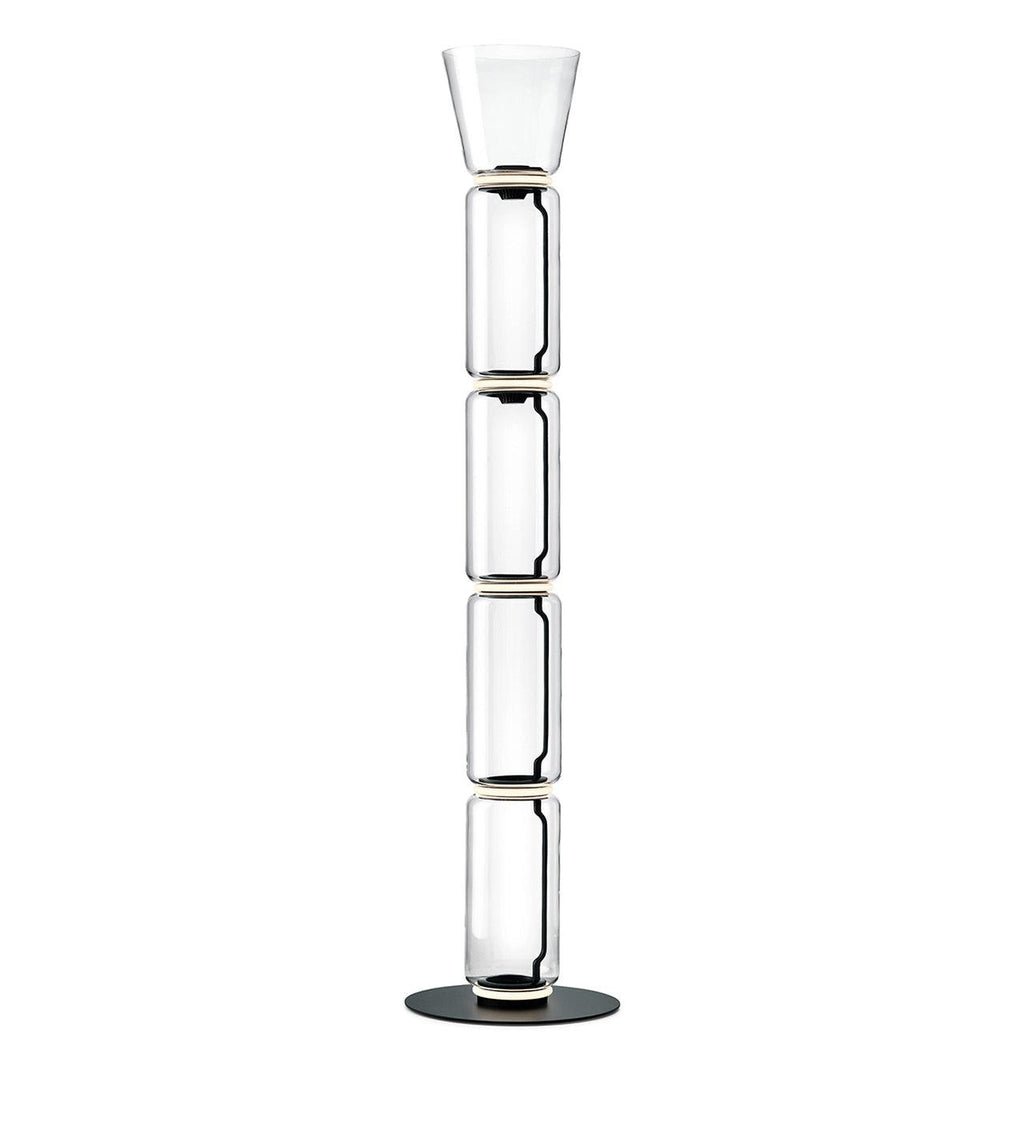 A Clérachic glass floor lamp with a narrow cone shade over four clear cylinders and a black round base, on white.