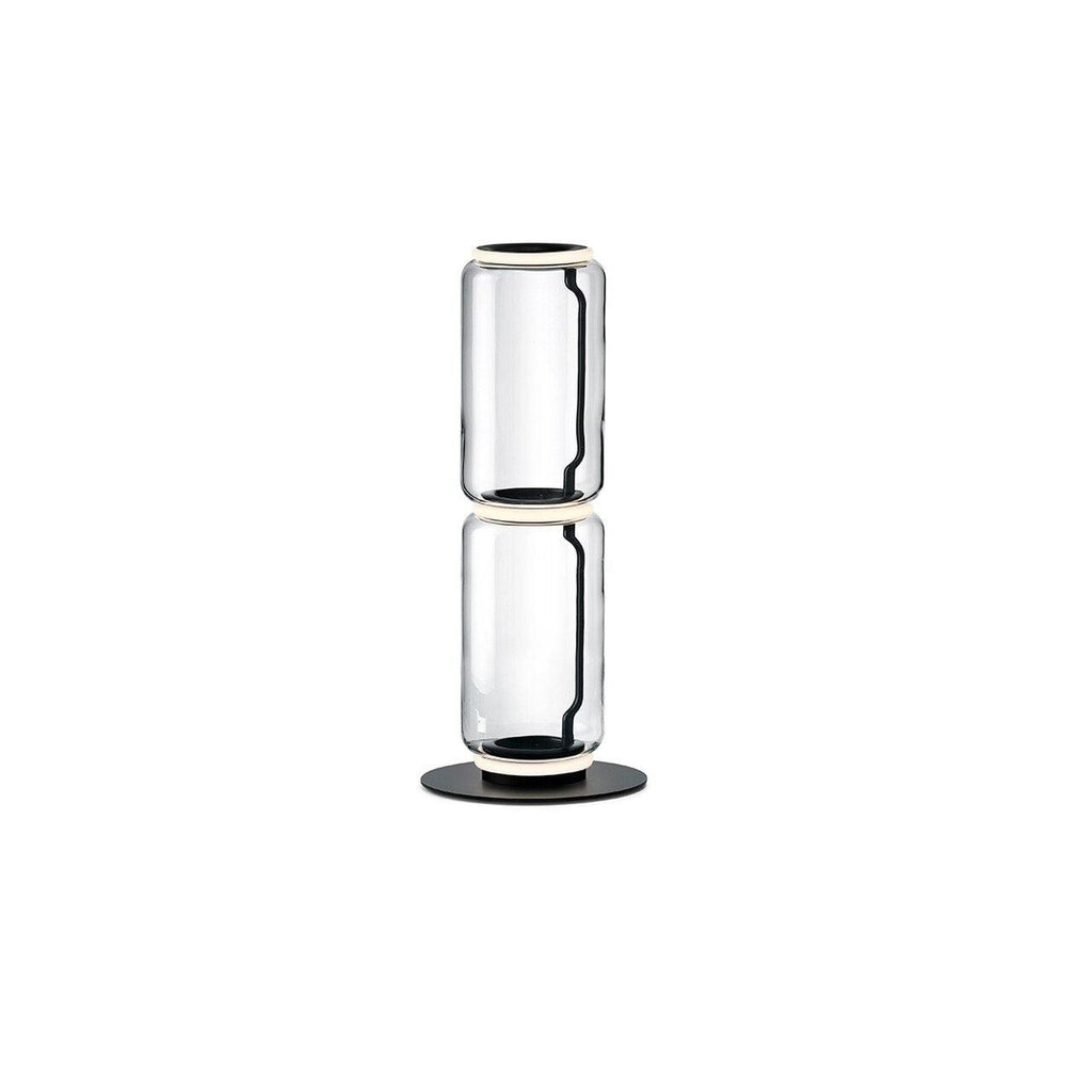Clérachic glass lamp with two stacked clear cylinders and a ring of light at the top, on a round black base against white.