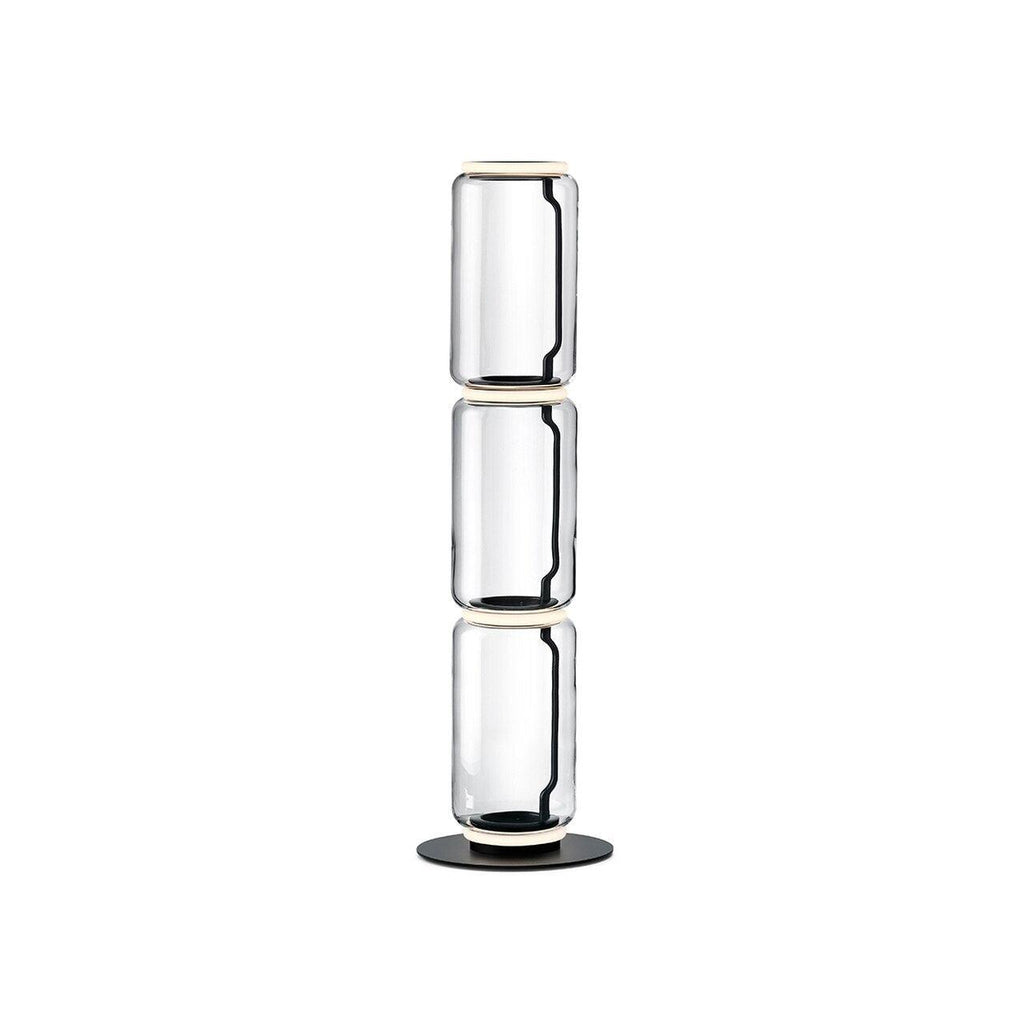 Clérachic glass floor lamp with three stacked clear cylinders and a ring at the top, on a black round base against white.