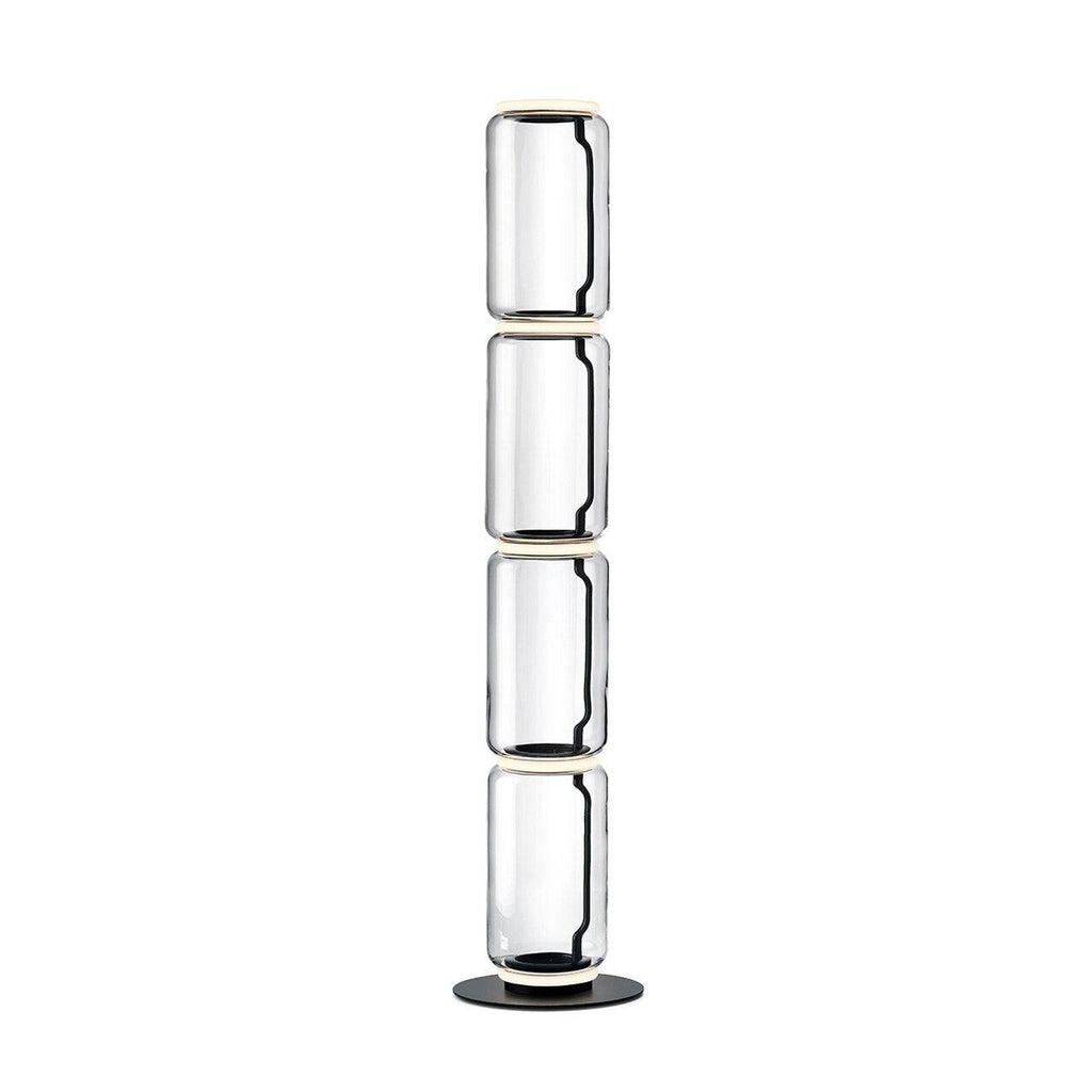 Clérachic glass floor lamp with four stacked clear cylinders and a black cord inside, on a round black base against white.