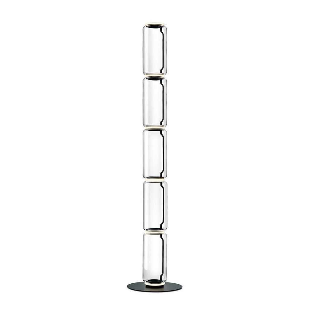 Tall Clérachic glass floor lamp made of five narrow clear cylinders, stacked on a round black base against white.