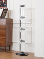 Unlit Clérachic glass floor lamp beside a walnut chest with a framed floral picture, against a white panelled wall.