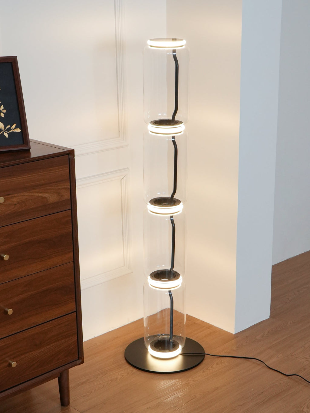 Lit Clérachic glass floor lamp at the edge of a walnut chest, warm light ringing each joint and shining on the base.