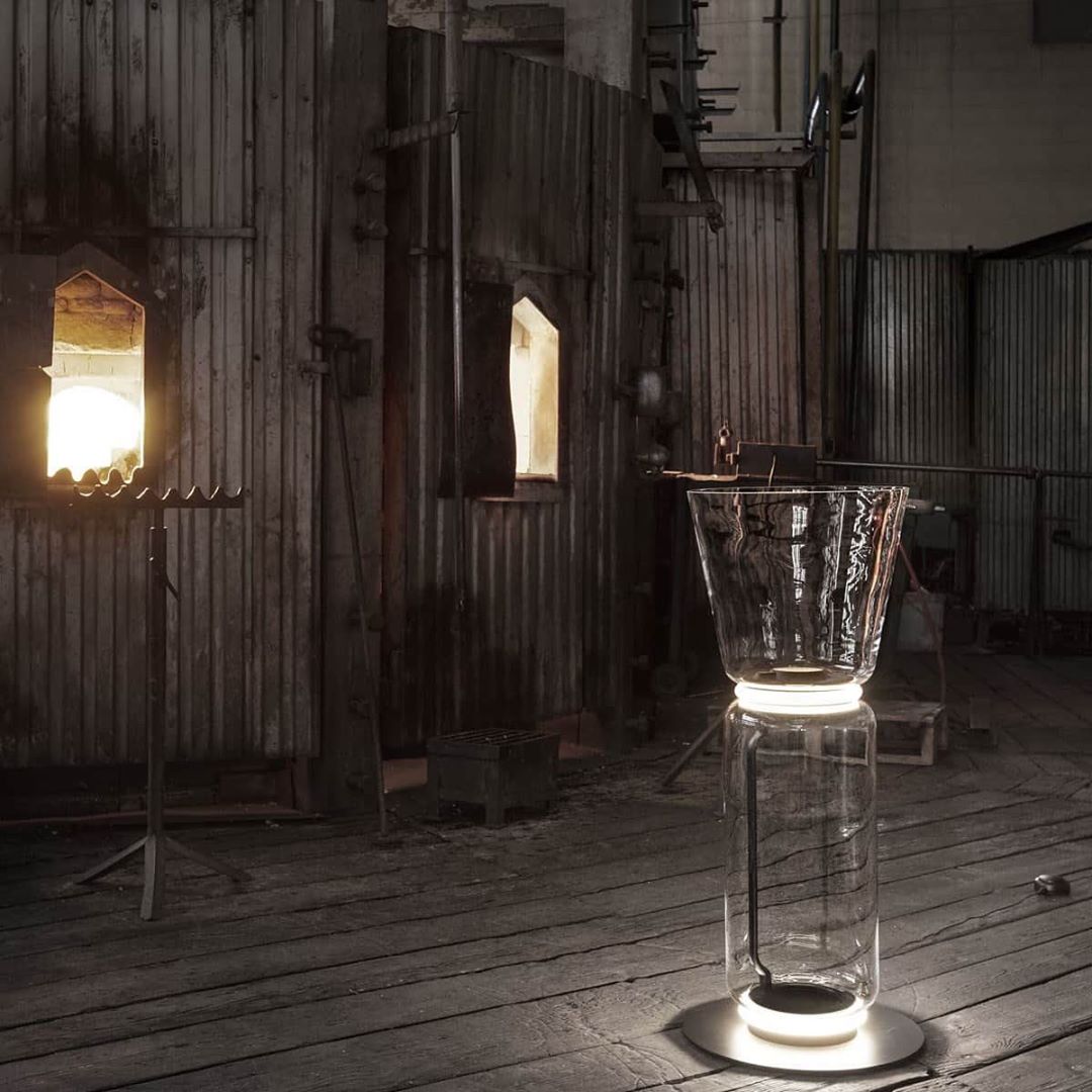 Clérachic glass floor lamp with a cone shade on a plank floor in a timber-walled space, with a lit window opening behind it.
