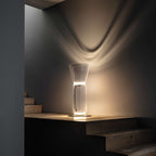 Short Clérachic glass floor lamp with a cone shade on a wooden step, throwing a wave of warm light up a dark wall.