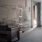 A Clérachic glass floor lamp with a bowl shade in a hall with ornate walls, beside a dark leather and wood sofa and an open doorway.
