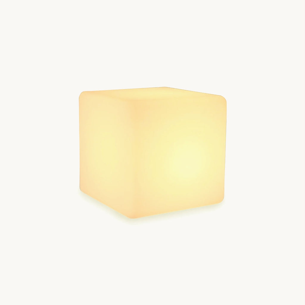 A glowing white cube-shaped Clérachic floor lamp with softly rounded corners, lit warm, on a plain white backdrop.