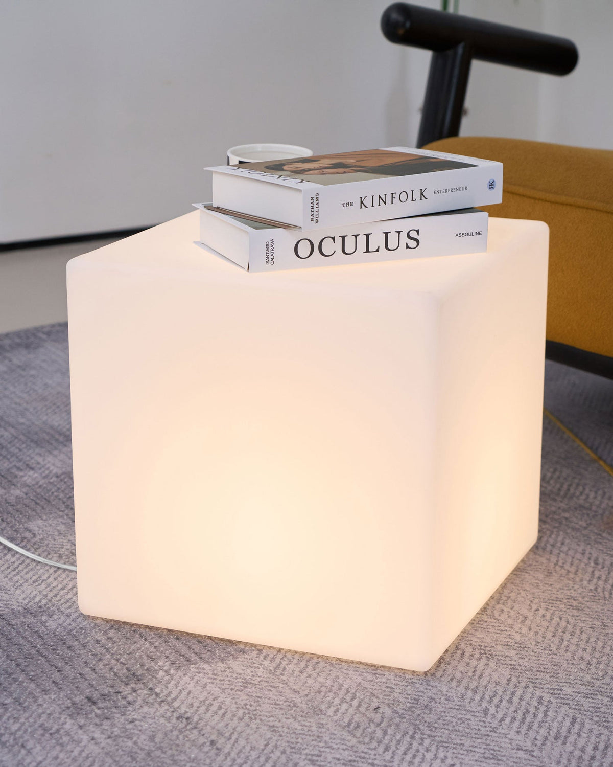 Two design books and a small dish rest on top of this white Clérachic cube lamp, which stands on a grey rug.