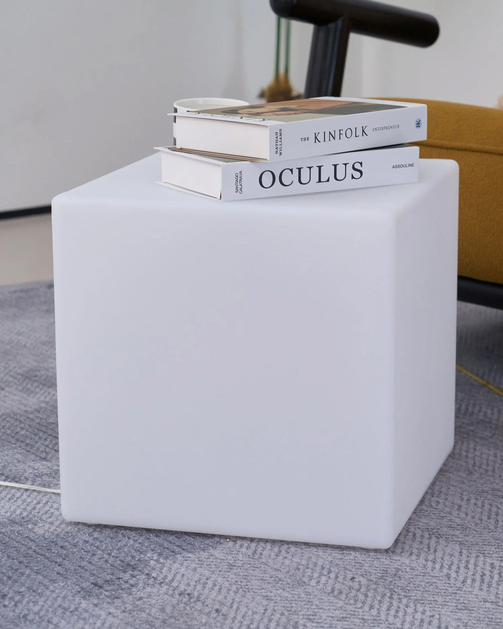 An unlit white Clérachic cube lamp on a grey rug, with two design books stacked on top of it.