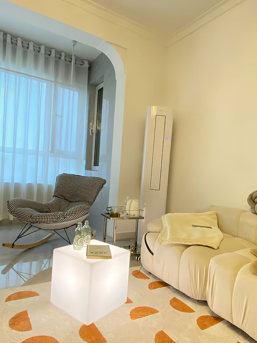 A white Clérachic cube lamp used as a side table, with a glass vase on top, in a cream living room with a rocking chair.