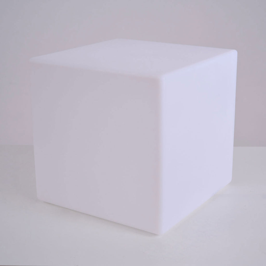 A white Clérachic cube lamp, unlit, with softly rounded edges, on a pale surface against a grey wall.