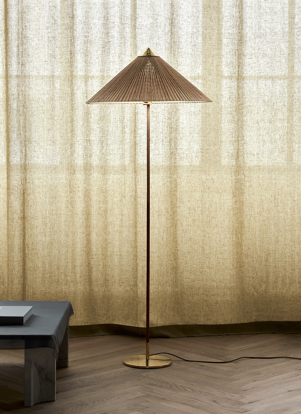 Clérachic floor lamp with a natural woven conical shade in front of a floor-length linen curtain, with a low stone bench beside it.