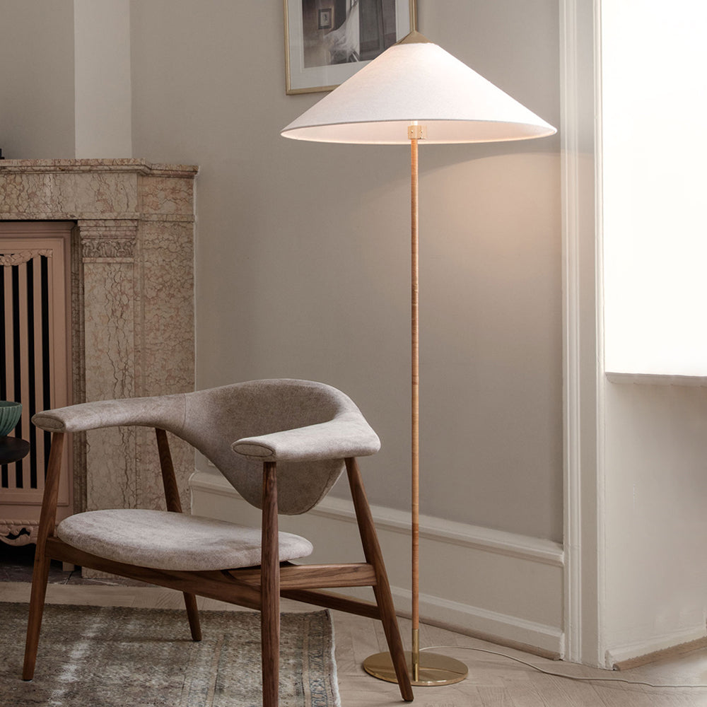 Shown here, a Clérachic floor lamp with a white fabric conical shade glows beside a wooden armchair, in front of a stone fireplace.