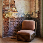 In this photo, a Clérachic floor lamp with a floral printed shade stands in a corner of exposed brick, next to a rust-pink armchair with a ribbed base.