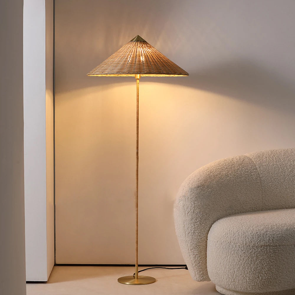 Warm light from this Clérachic floor lamp with a natural rattan shade falls on a cream wall, beside a rounded boucle armchair.