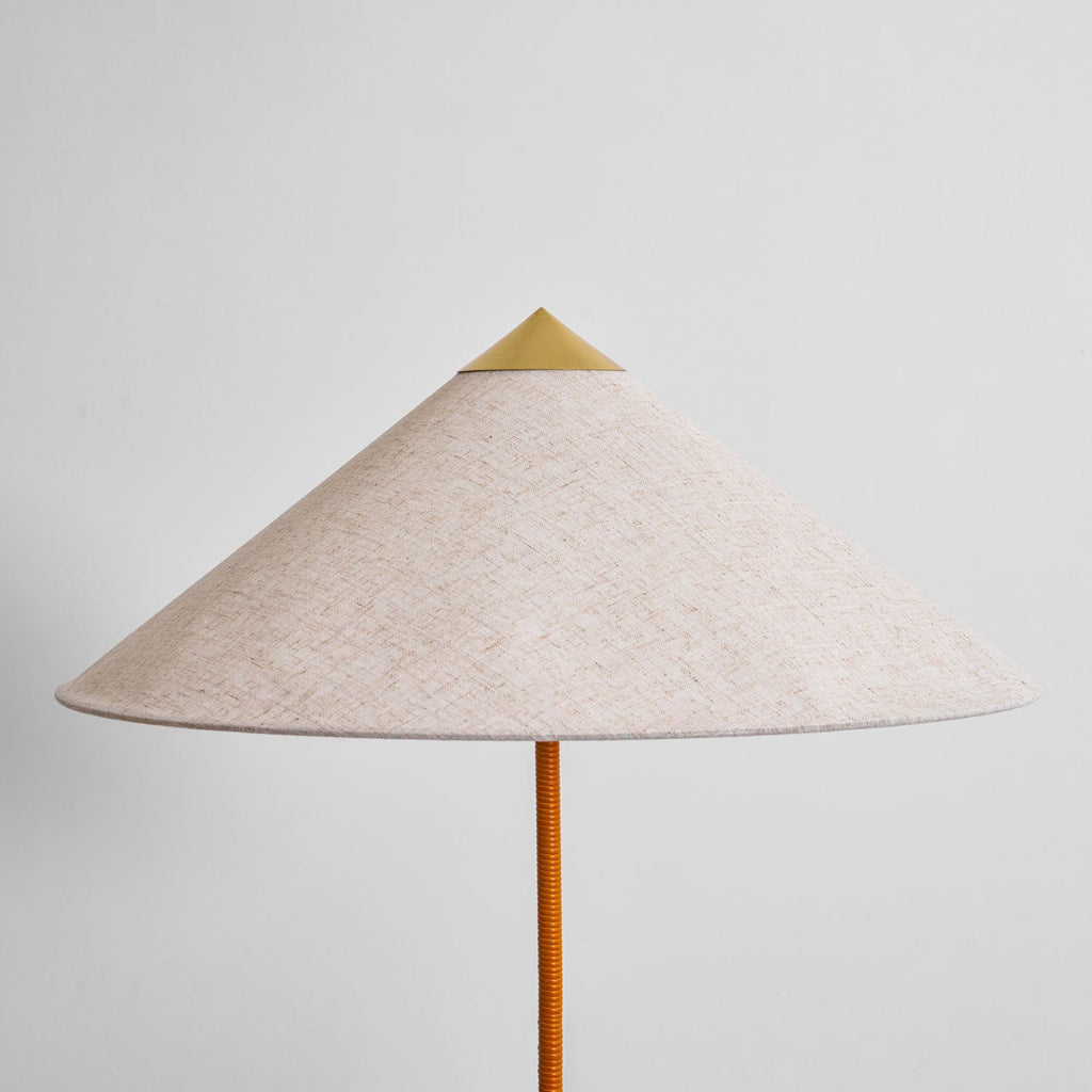 Close view of the natural linen-look shade and brass cap on this Clérachic floor lamp, above a tan cane-wrapped stem.