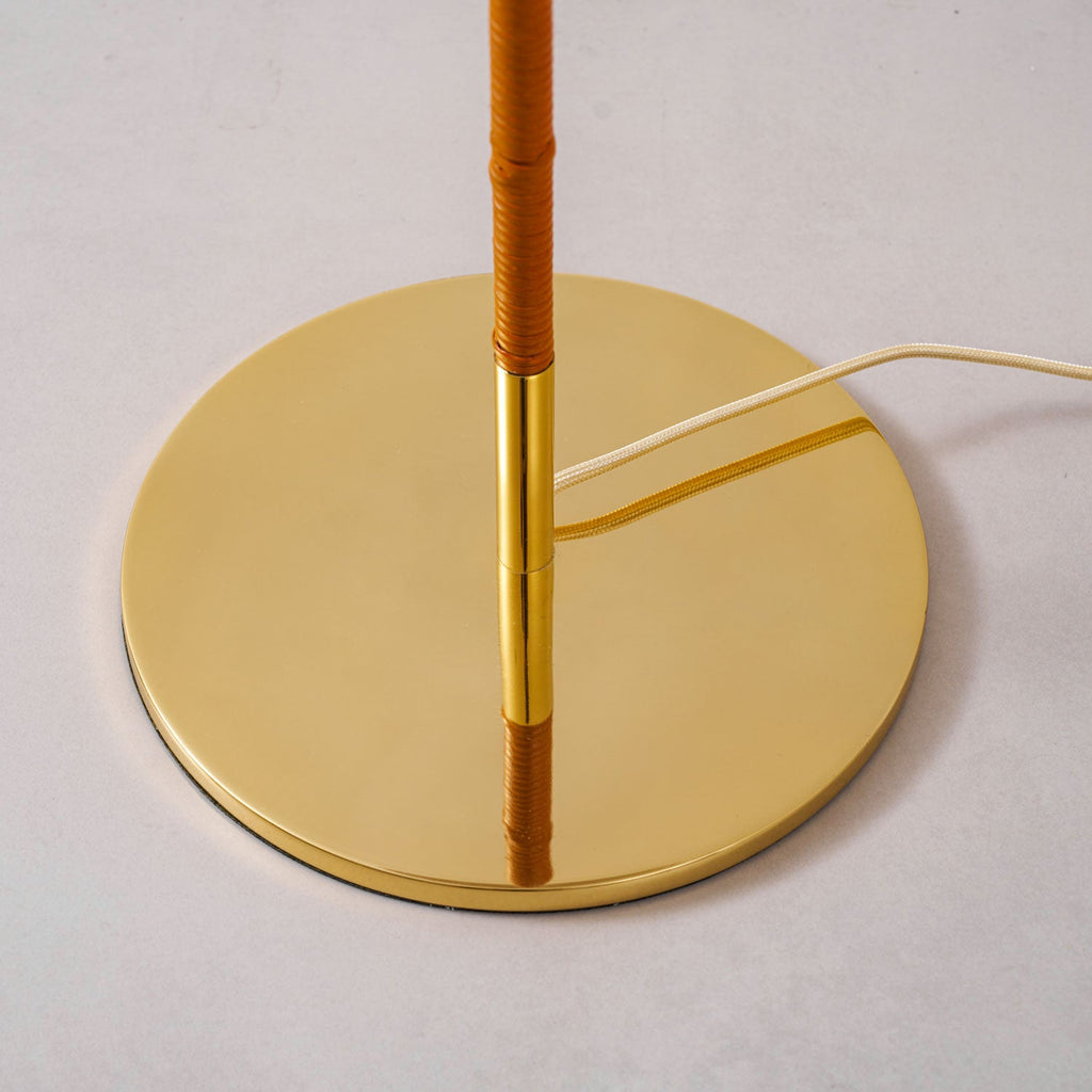 Close view of the round polished brass base of this Clérachic floor lamp, where the tan wrapped stem meets a brass collar.