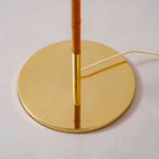Close view of the round polished brass base of this Clérachic floor lamp, where the tan wrapped stem meets a brass collar.